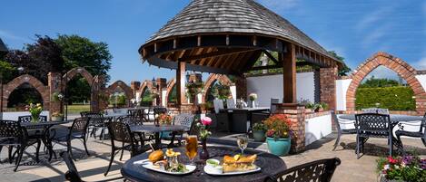 An outdoor patio with brick arches, a gazebo, and tables with chairs.