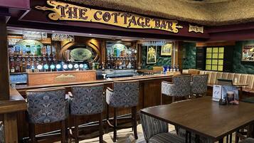 A bar area with a sign reading 'The Cottage Bar,' featuring a bar counter, multiple stools, and a table with chairs.