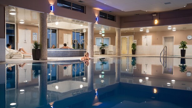 Ein großer, überdachter Pool mit klarem Wasser, umgeben von Liegestühlen und Topfpflanzen.