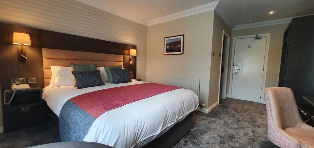 Una habitación de hotel con una cama grande, lámparas de noche, una silla y una puerta.