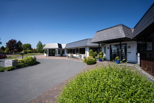 A modern building with a curved driveway, outdoor seating area, and well-maintained landscaping. - Burrendale Hotel Country Club & Spa (Newcastle)