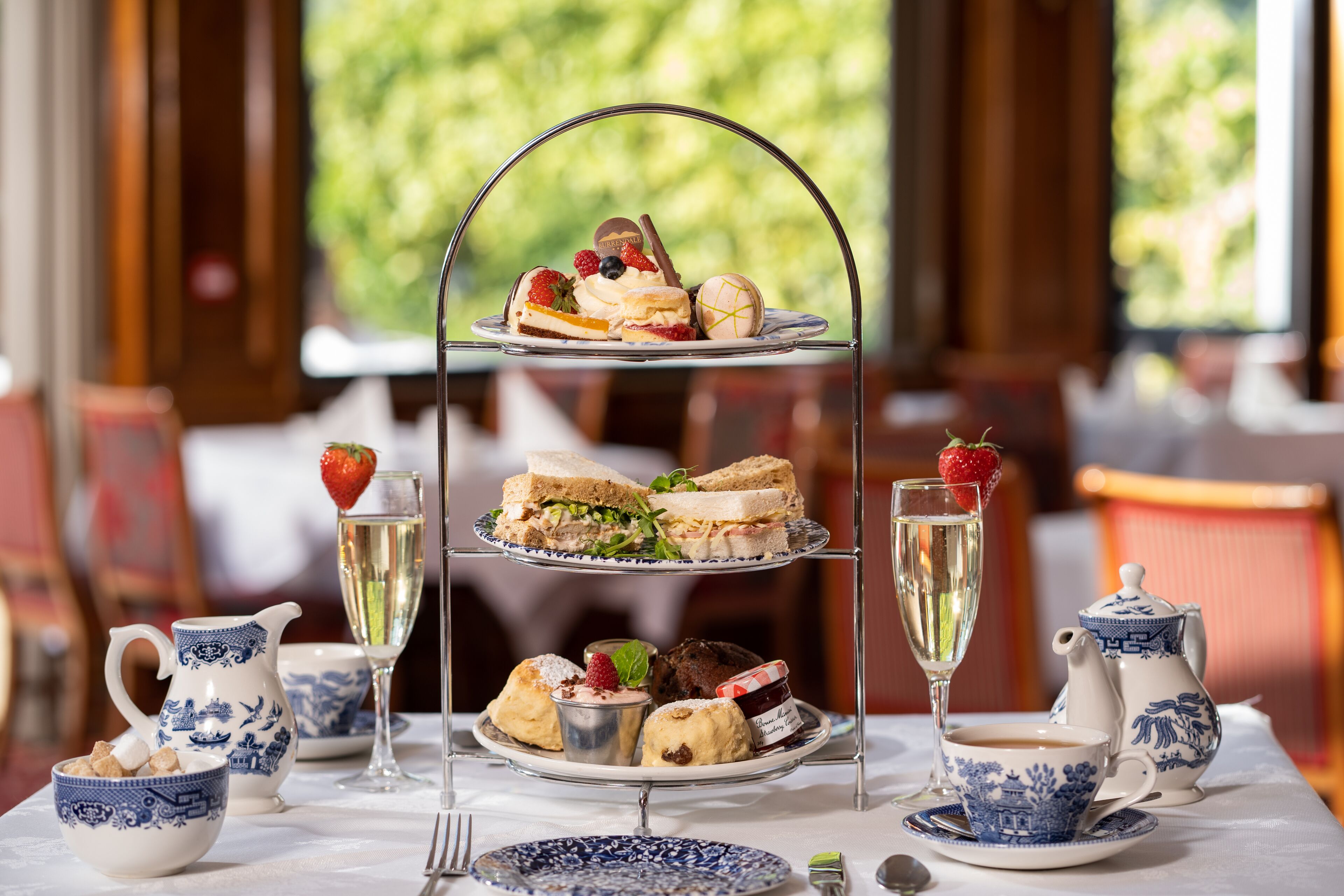 A three-tiered dessert stand with various pastries and sandwiches, accompanied by tea service and a pitcher of champagne.