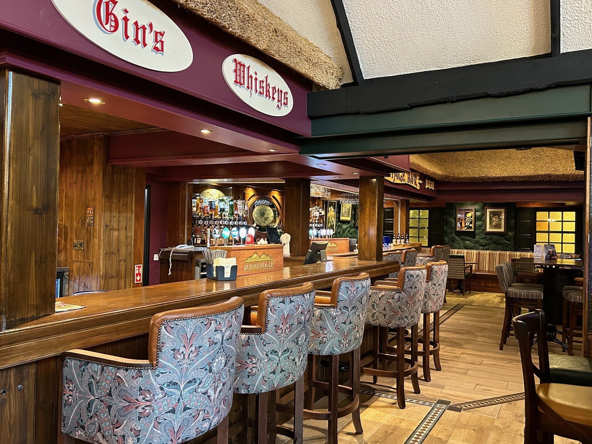 A bar area with a long counter, bar stools, and a variety of bottles and glasses.