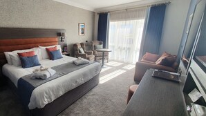 Ein Hotelzimmer mit einem großen Bett, einem Schreibtisch, einem Stuhl und einem Balkon mit Vorhängen.
