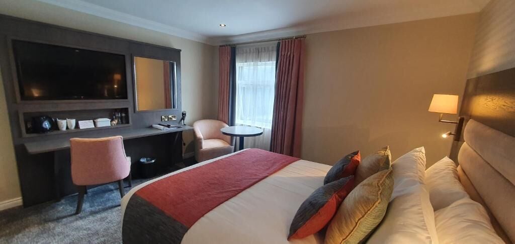 A hotel room with a bed, a desk, a chair, a TV, and a lamp.