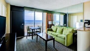 A hotel room with a balcony, a green sofa, a dining table, and a TV. - Bch Q 1BR 1BA w Ocean Front Balcony - sleeps 6 (Virginia Beach)