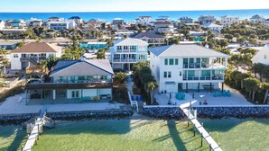 A coastal property with a large house featuring multiple balconies, a swimming pool, and a pier leading to the beach. - Stunning Waterfront Home w/ Private Saltwater Pool & beautiful Tiki Bar! (Pensacola Beach)