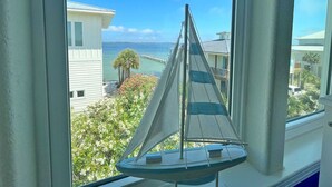 A sailboat model on a windowsill with a view of a coastal area and a jet formation in the sky. - Stunning Waterfront Home w/ Private Saltwater Pool & beautiful Tiki Bar! (Pensacola Beach)