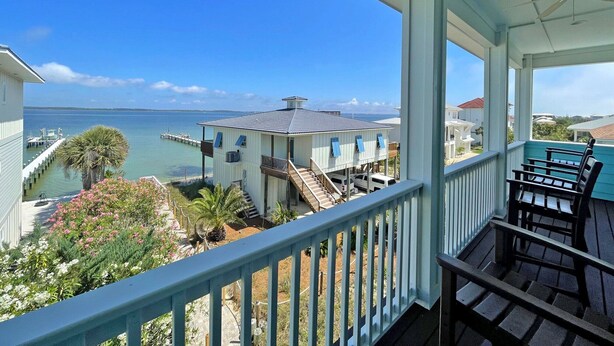 A covered balcony with a view of the sea, a dock, and neighboring houses. - Stunning Waterfront Home w/ Private Saltwater Pool & beautiful Tiki Bar! (Pensacola Beach)