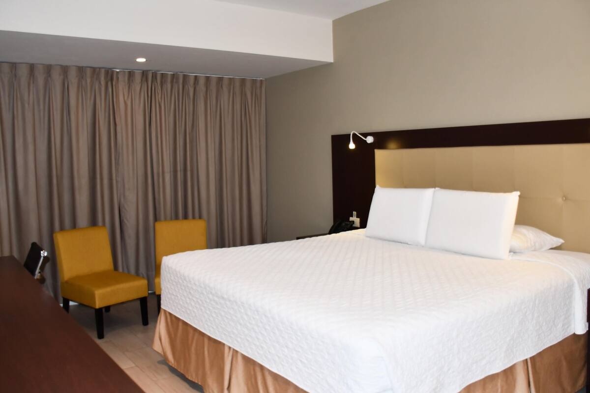 Una habitación de hotel con una cama grande, una silla, una mesita de noche y una lámpara.