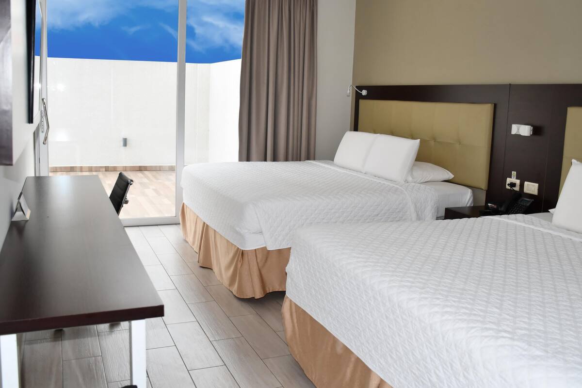 Habitación de hotel con dos camas, un escritorio, un teléfono y vista al cielo.