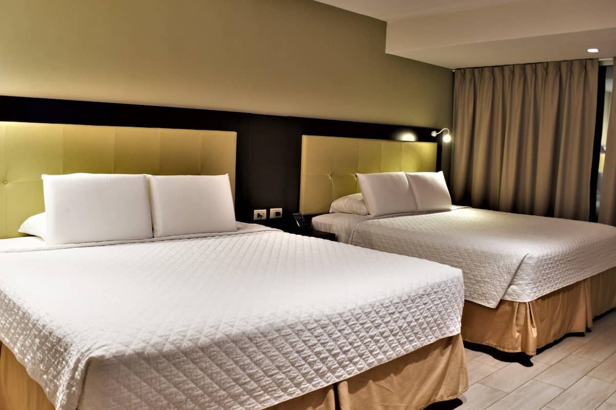 Habitación de hotel con dos camas, cada una con ropa de cama blanca y cabeceros.