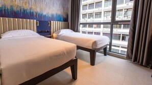 Ein Hotelzimmer mit zwei Betten, einem großen Fenster mit Vorhängen und einem modernen, abstrakten Gemälde an der Wand.