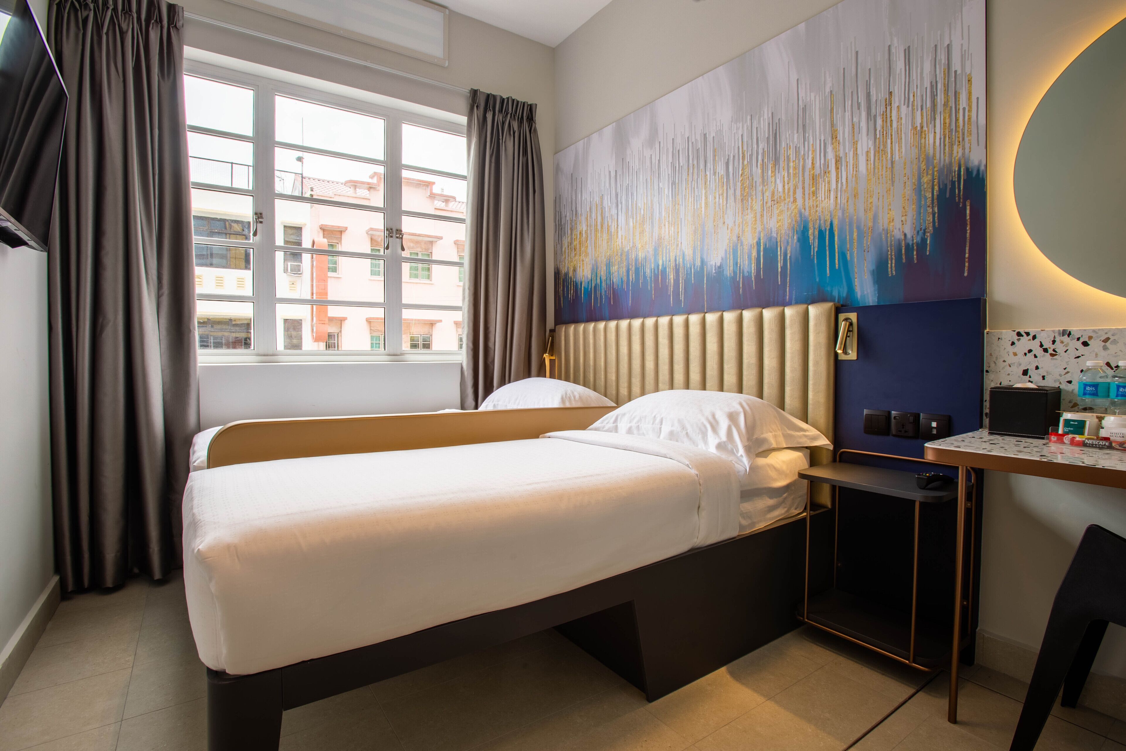 Habitación de hotel con cama, escritorio y silla, un cuadro abstracto grande en la pared y una ventana con cortinas.