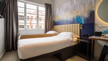 Habitación de hotel con cama, escritorio y silla, un cuadro abstracto grande en la pared y una ventana con cortinas.