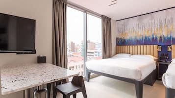 Une chambre d’hôtel avec un lit, un bureau, une chaise, une télévision et un tableau au mur.