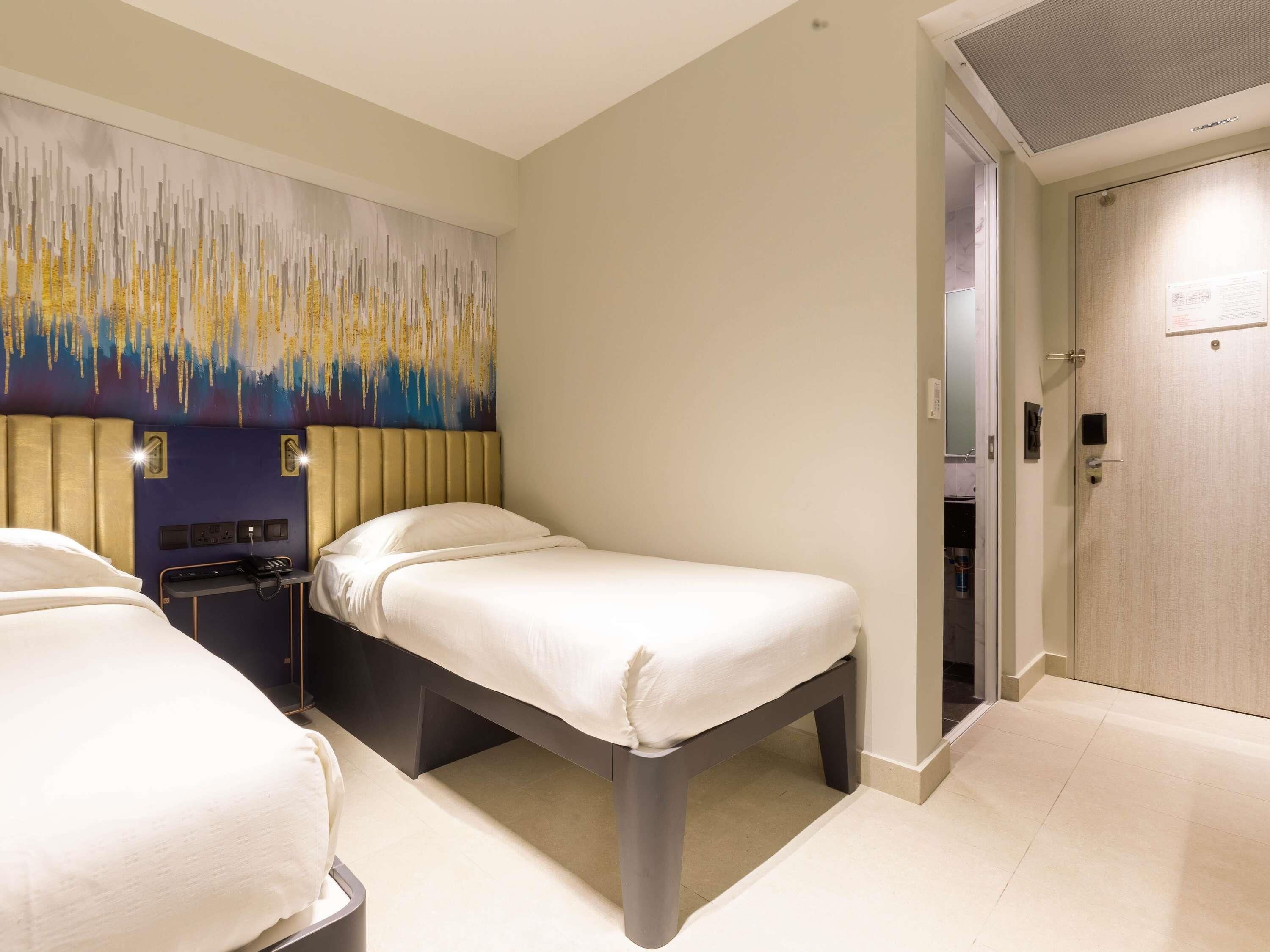 A hotel room with two beds, a modern headboard, a wall art piece, and a door with a lock.