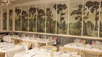 Un espace repas avec des tables dressées pour le service, une grande fresque représentant une forêt sur le mur et un lustre.