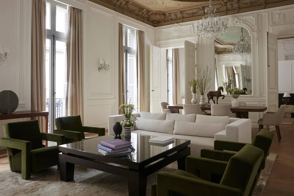A spacious living room with a white sofa, green chairs, a glass coffee table, and a chandelier.
