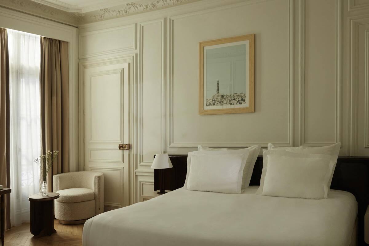 A hotel room with a large bed, a chair, a bedside table, and a framed picture on the wall.