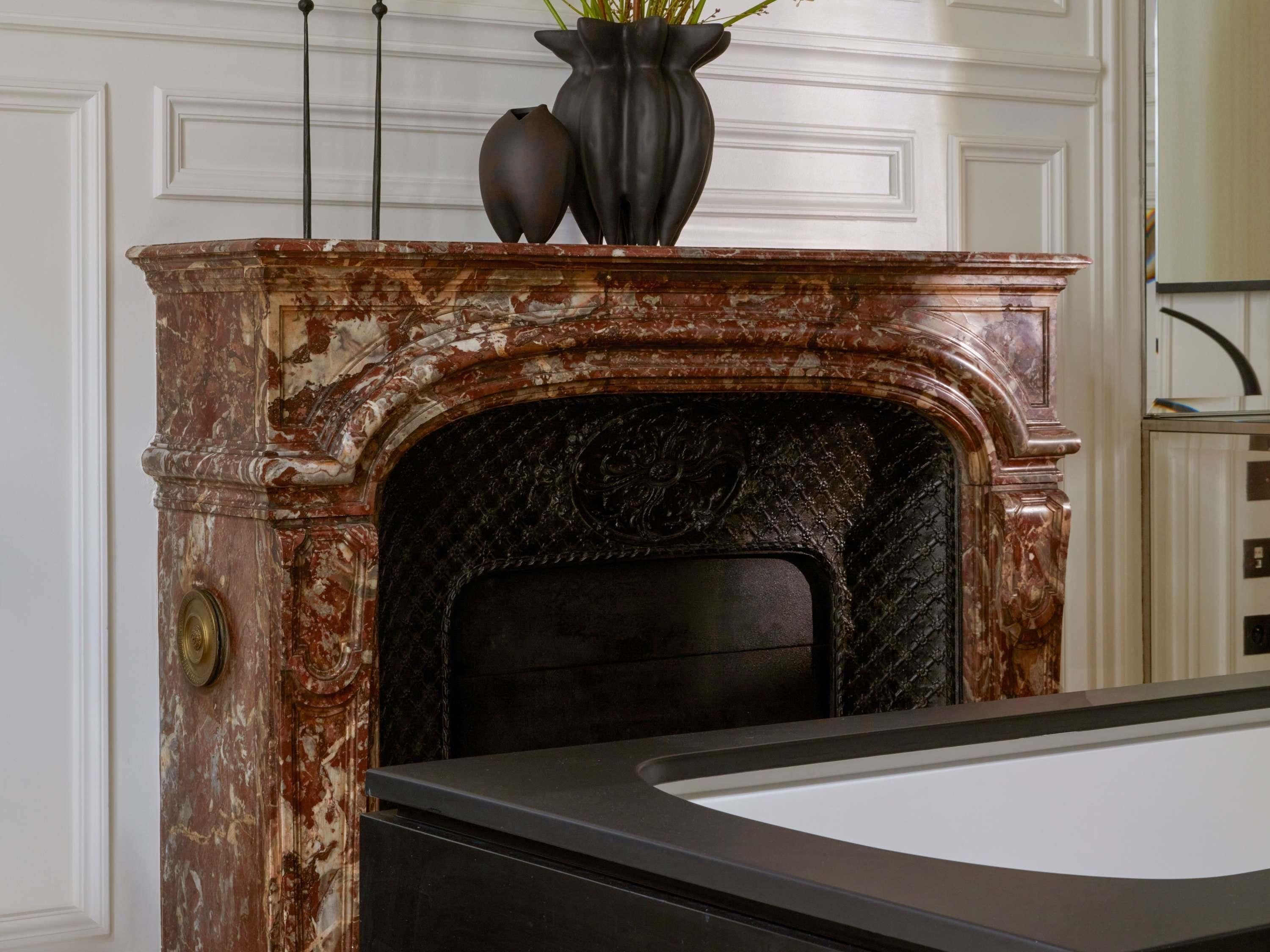 A fireplace with a marble surround, a black mantelpiece, and a vase with plants on top.