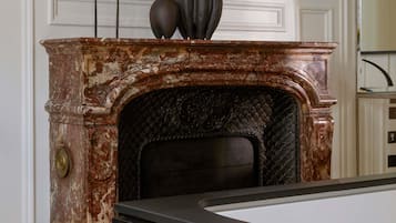 A fireplace with a marble surround, a black mantelpiece, and a vase with plants on top.