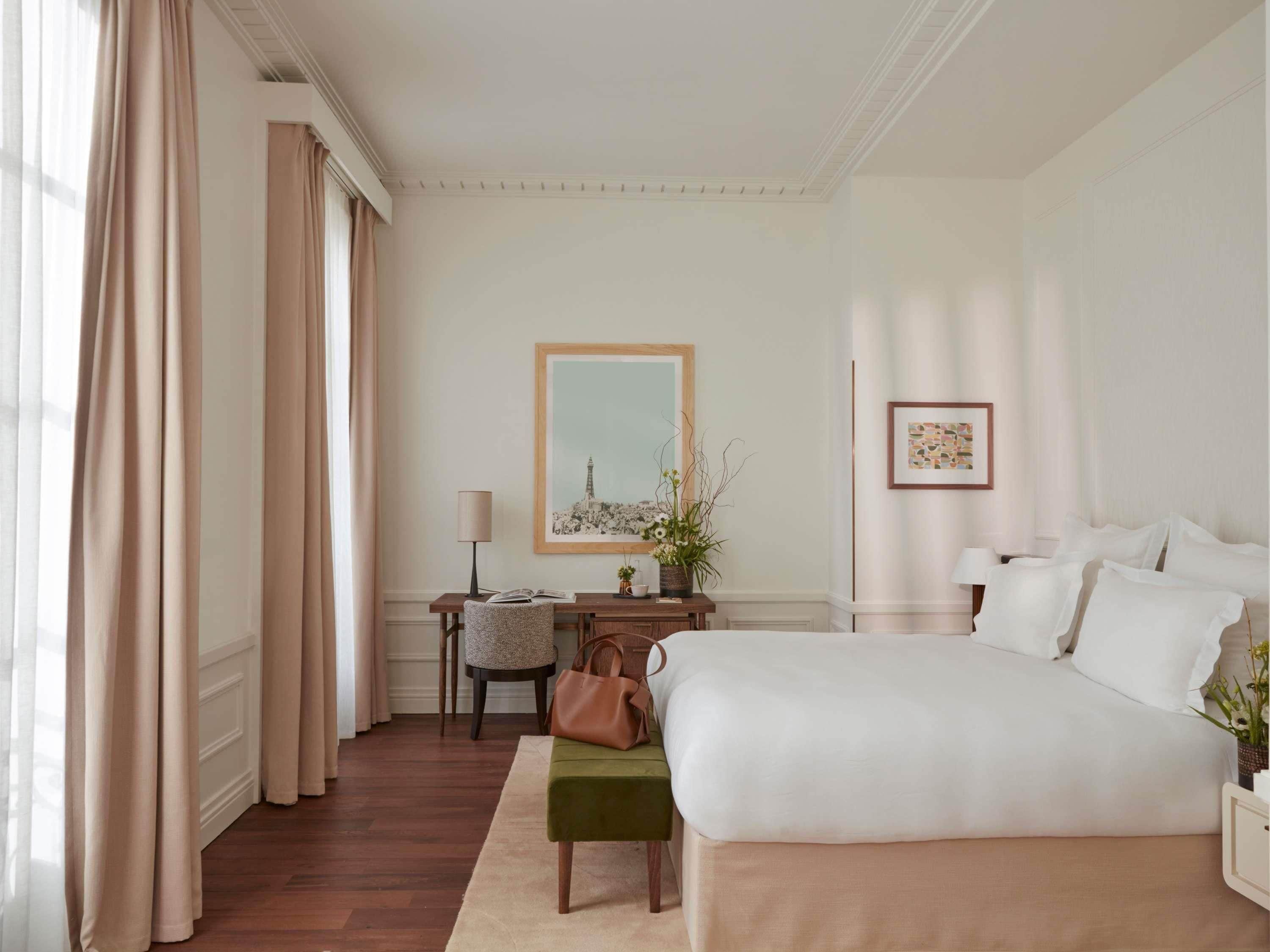 A hotel room with a bed, a desk, a chair, a lamp, and a framed picture on the wall.