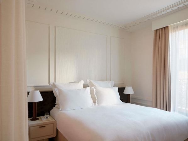 A hotel room with a bed, two bedside tables, a lamp, and a window with curtains.