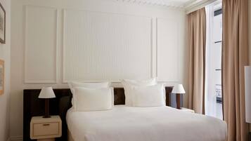 A hotel room with a large bed, two bedside tables with lamps, a large window with curtains, and a wall with paneling.