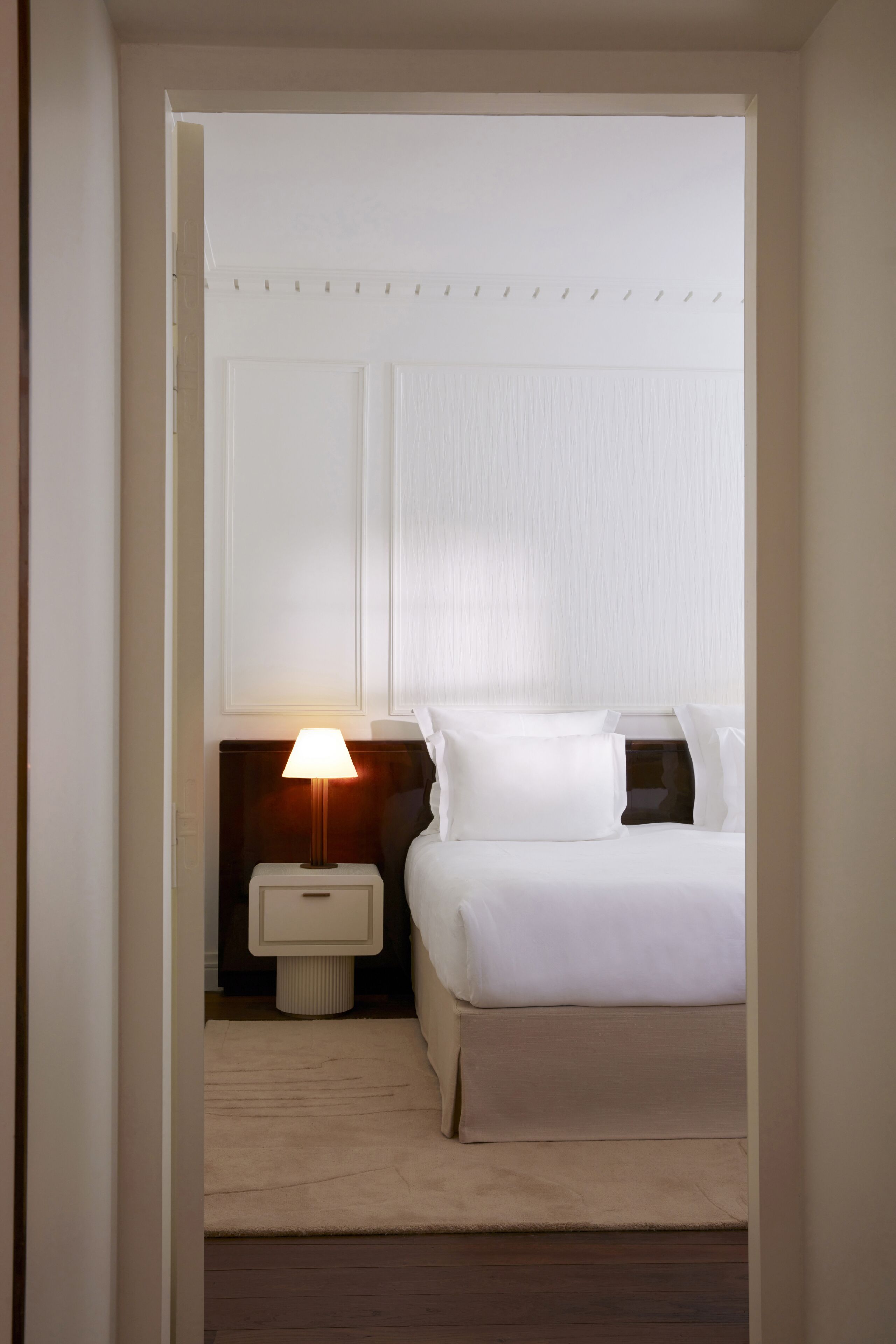 A hotel room with a bed, a nightstand, a lamp, and a window with blinds.