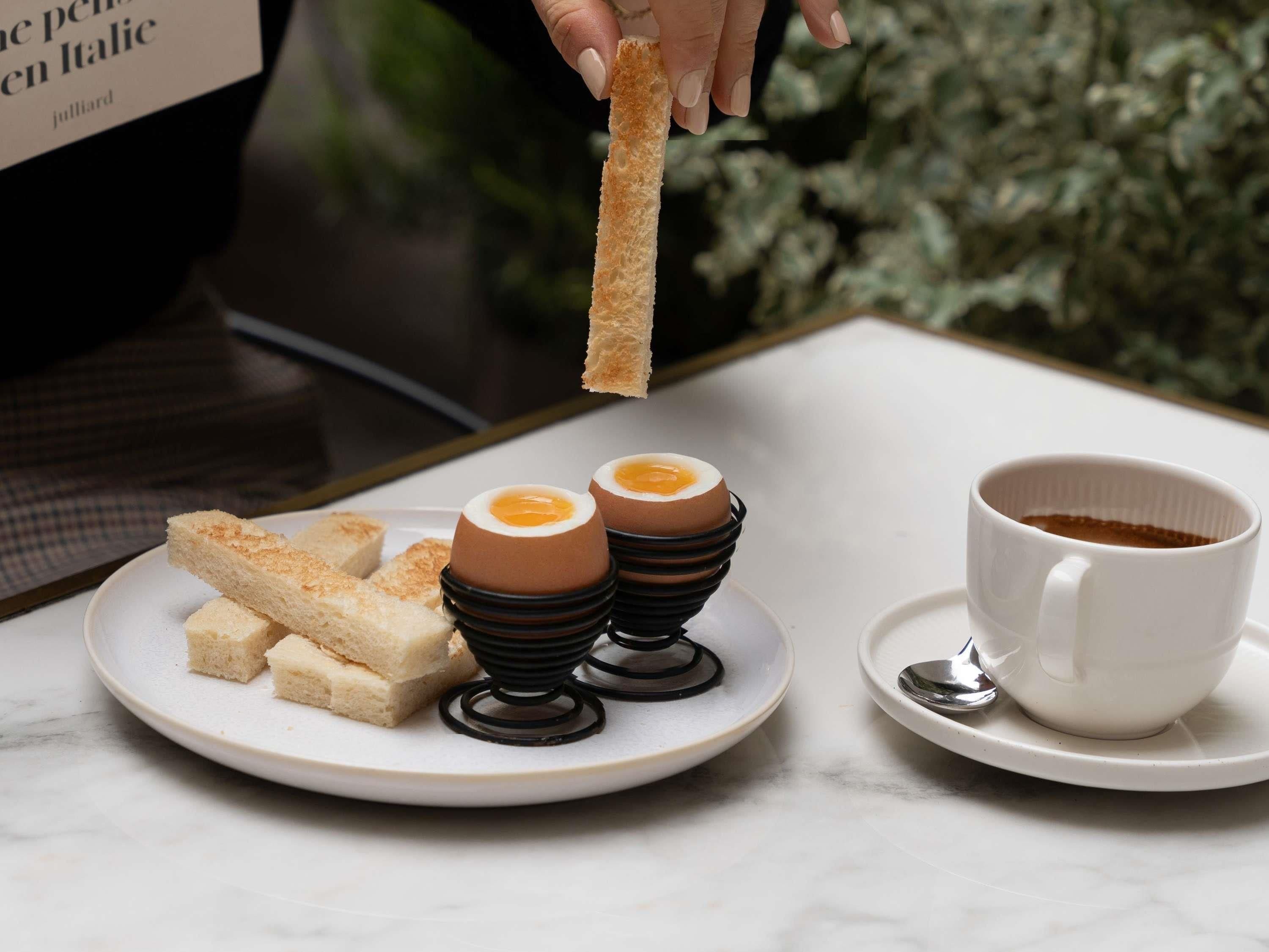 Une assiette avec des tartines, deux œufs au chocolat et une tasse de café, le tout posé sur une table.