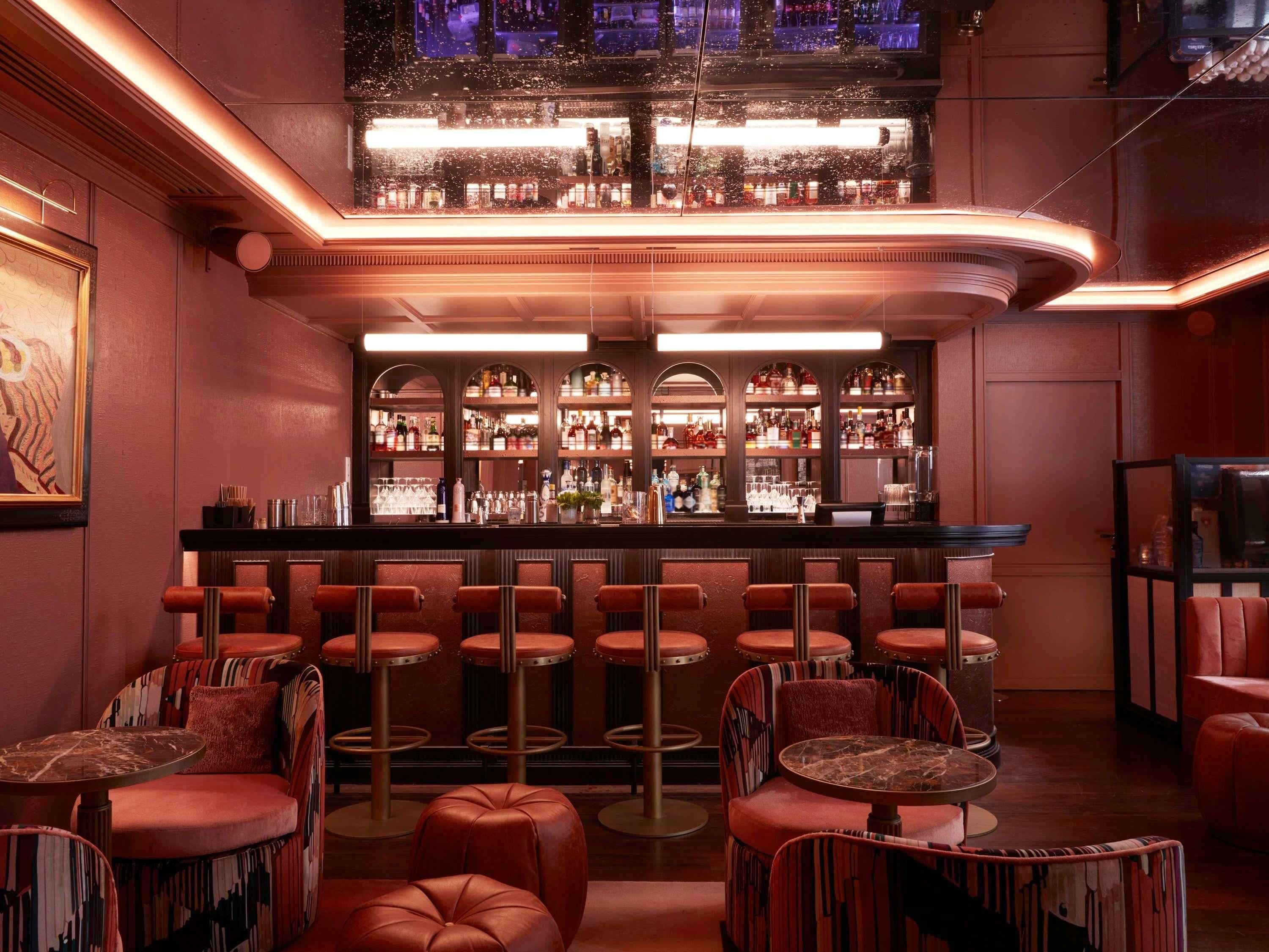 A bar area with multiple stools and a bar counter, shelves with bottles, and a ceiling light fixture.