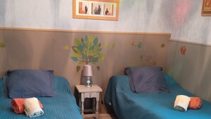 Une chambre avec deux lits, chacun recouvert d’une couverture bleue et agrémenté d’oreillers, une petite table de chevet avec une lampe, et un cadre photo fixé au mur.