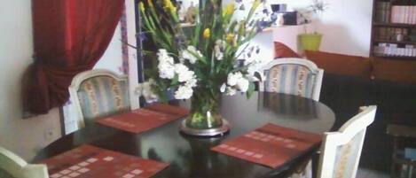 A dining table with a vase of flowers, surrounded by chairs.