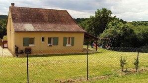 Une maison à deux étages avec un toit en pente, une cour clôturée et un ensemble de jeux avec une balançoire.