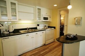 Kitchen features a stove, microwave, and coffee maker, with a small table and wooden floor.