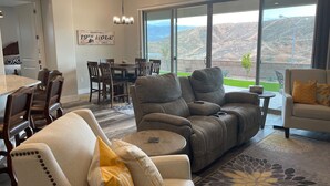 Amplia sala de estar con un ventanal que ofrece vistas a la montaña, comedor con mobiliario de madera y zona de estar acogedora con un sillón reclinable y un sofá.