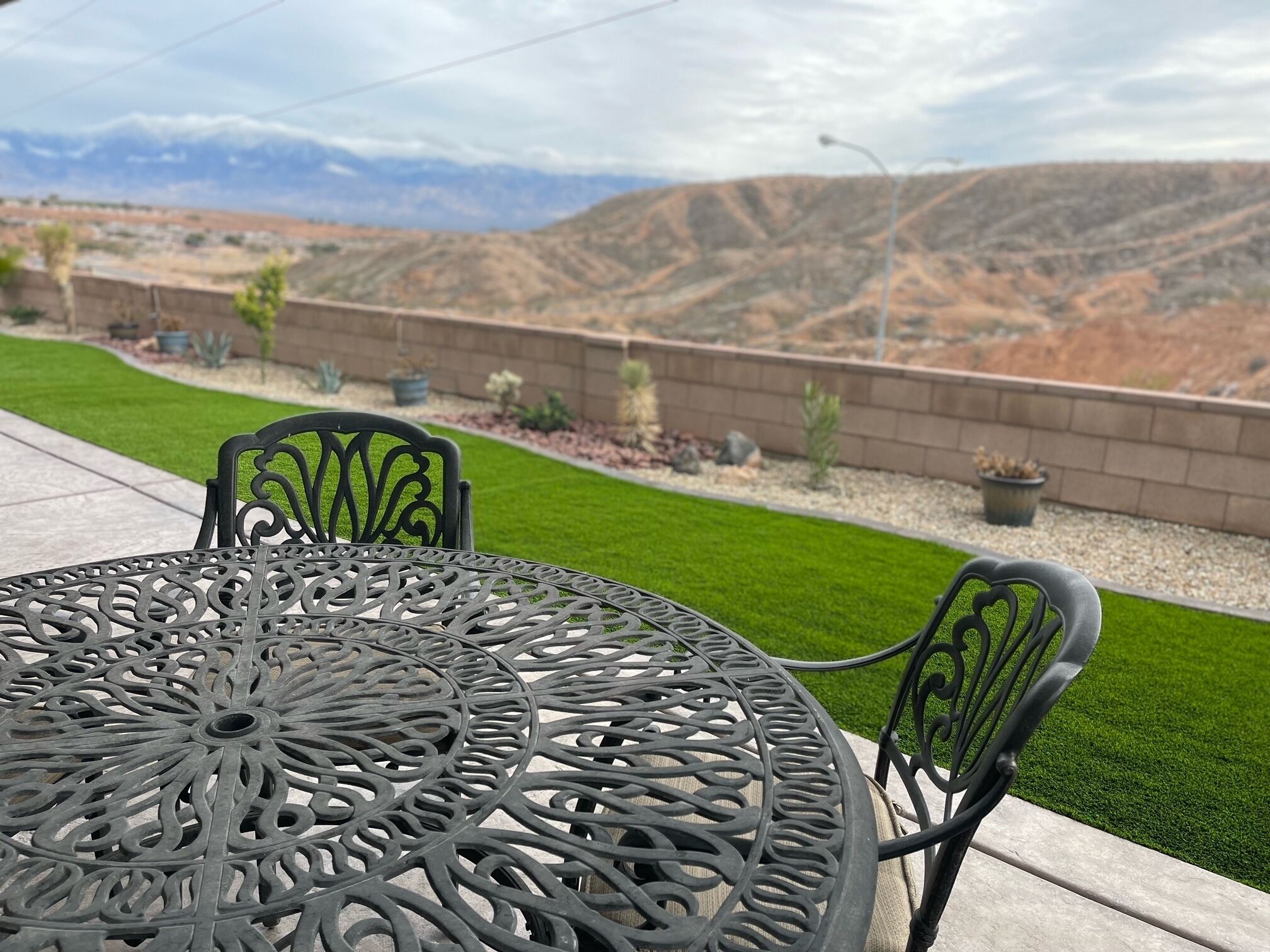 A round metal table with intricate designs, accompanied by two chairs, set on a patio with a view of a mountainous landscape.