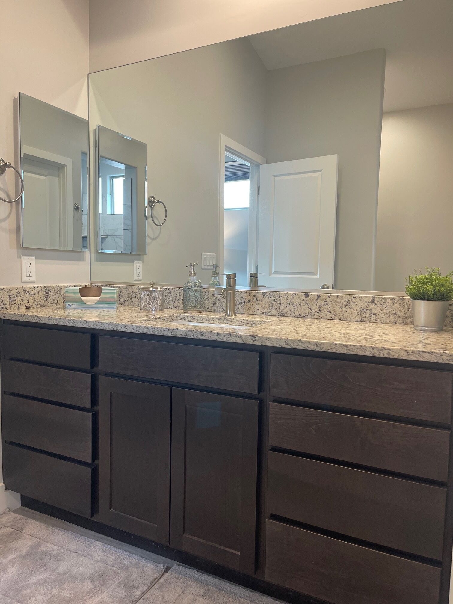 A modern bathroom with a large mirror, dark cabinetry, and a granite countertop.
