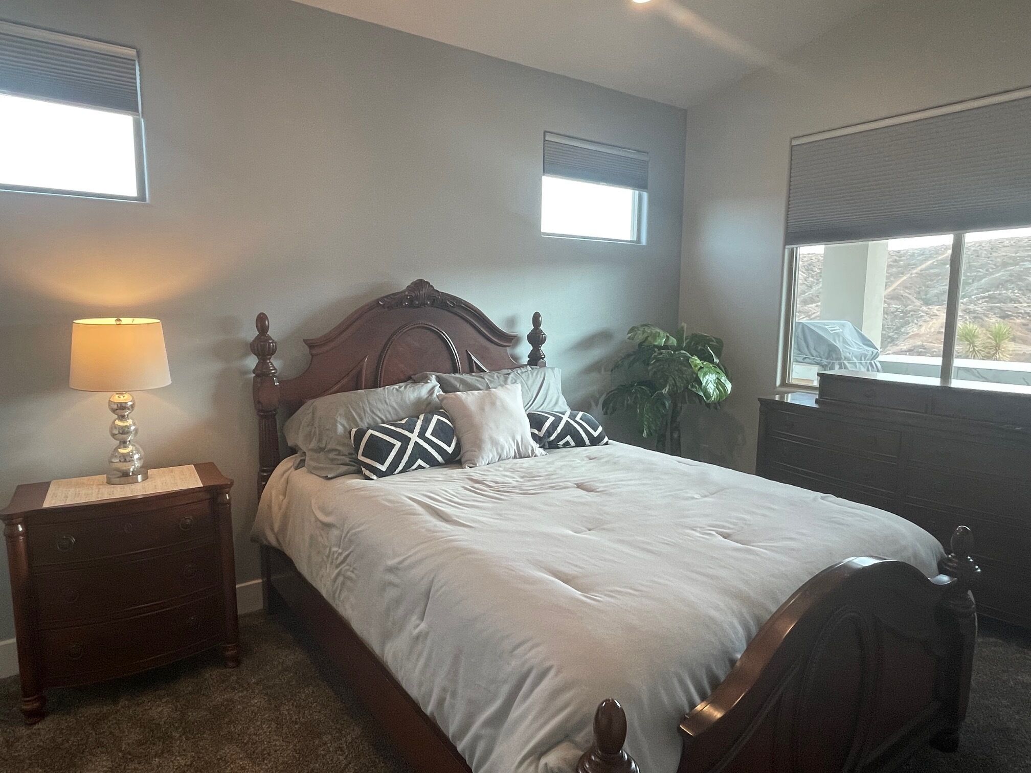 A bedroom with a wooden bed, a nightstand with a lamp, and a window with blinds.