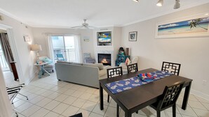 Uma sala de estar com sofá, mesa de jantar e cadeiras, lareira e ventilador de teto.