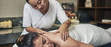 A massage therapy session in a spa setting with a massage table, towels, and a shelf with candles and decorative items.