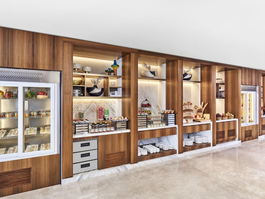Zona de servicio de alimentos con vitrinas refrigeradas, estanterías de madera y una encimera de mármol.
