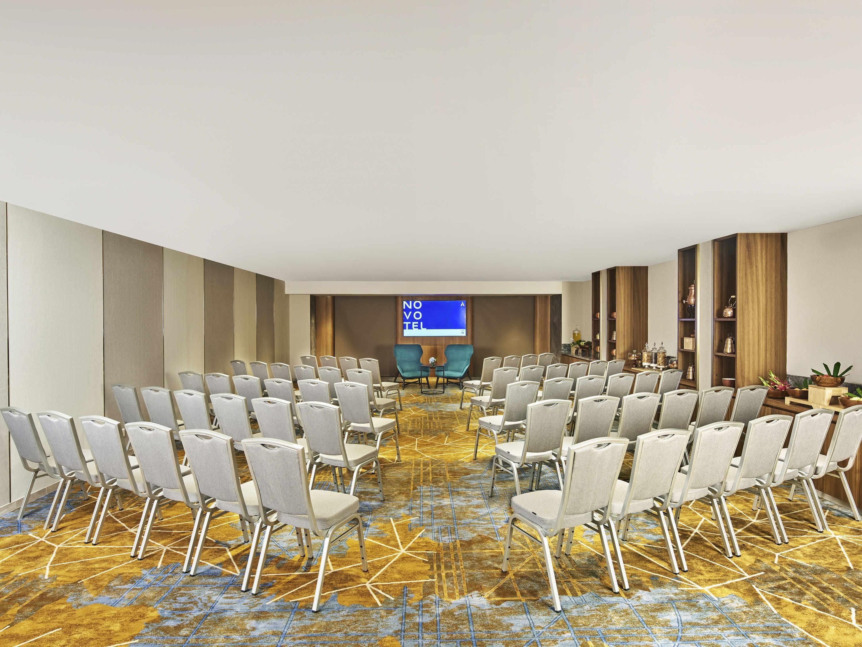 Ein Konferenzraum mit Stuhlreihen, einer Projektionsleinwand und einem Holzregal.