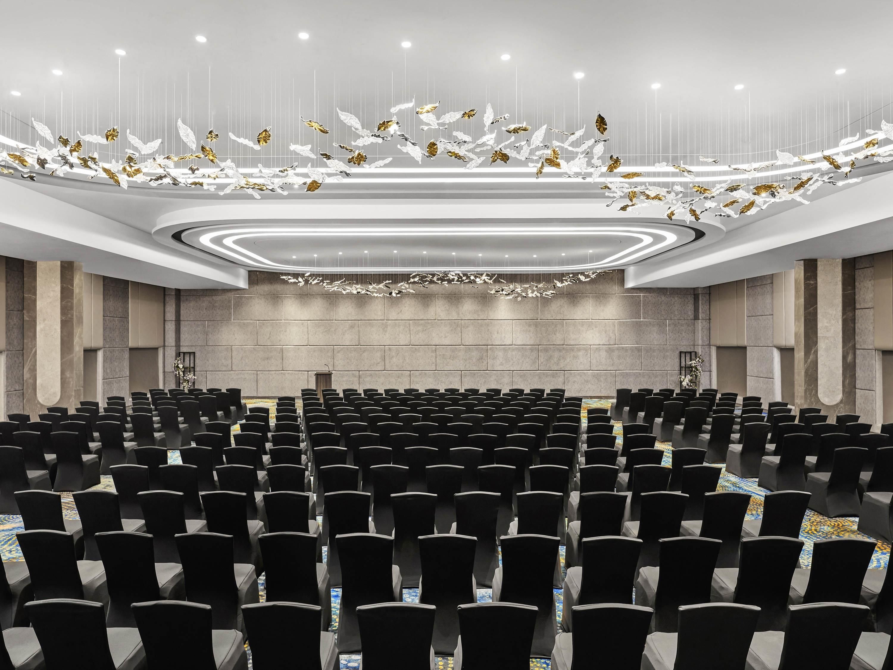 A conference room with rows of chairs, a podium, and a ceiling with hanging decorative elements.