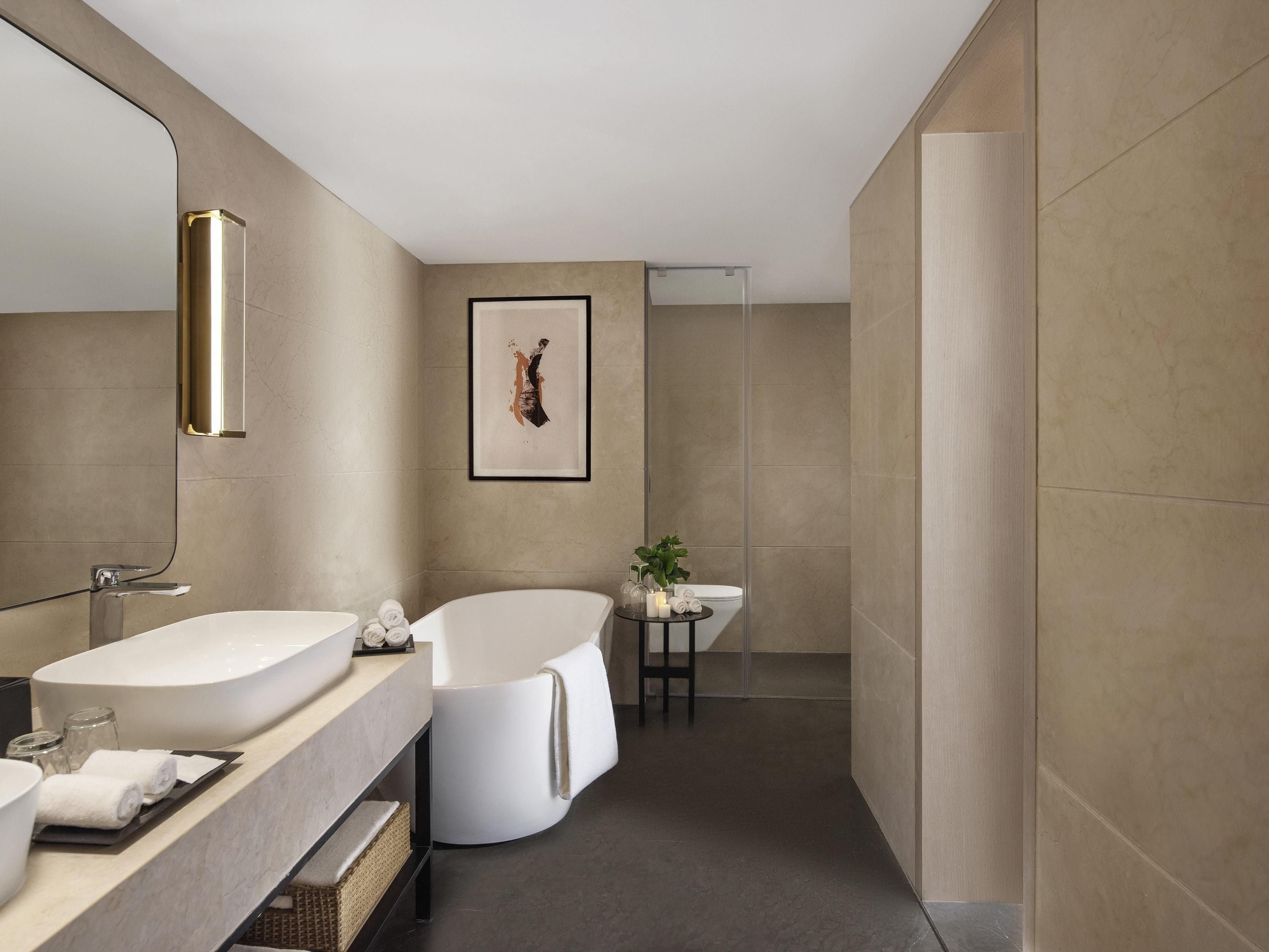 A modern bathroom with a freestanding bathtub, a large mirror, and a framed artwork on the wall.