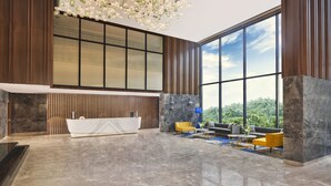 A modern lobby with a reception desk, seating area, large windows, and a decorative ceiling light fixture. - Novotel Mumbai International Airport (Mumbai)
