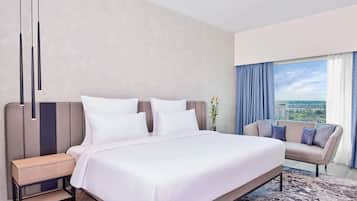 Habitación de hotel moderna con una cama grande, una mesita de noche, un sofá, vistas de la ciudad a través de la ventana y un florero con flores.