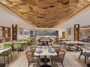 Un restaurante espacioso con varias zonas de comedor, una cocina central y un techo decorativo.