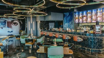 Zona de bar con mostrador de mármol, diversas opciones de asientos y un mural grande en la pared.